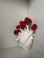 Heart-shaped vase with red flowers against a white wall